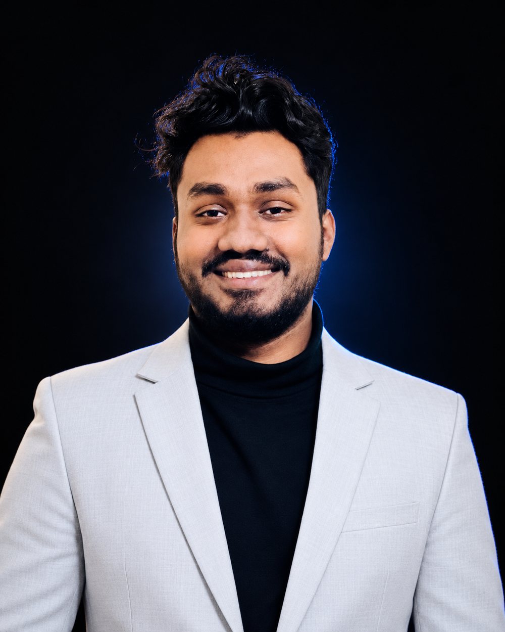Portrait of Amran H. Fahim smiling, wearing a light gray blazer over a black turtleneck